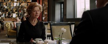 Movie still from “Woman in Gold” (2015), directed by Simon Curtis – An older woman sitting at a table with a flower in a vase; Medium shot, Over the shoulder angle