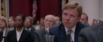 Movie still from “Woman in Gold” (2015), directed by Simon Curtis – A man in a suit and tie sitting in front of other men; Close Up shot, Over the shoulder angle