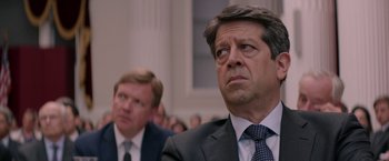 Movie still from “Woman in Gold” (2015), directed by Simon Curtis – A man in a suit and tie in front of another man in a suit and tie; Close Up shot, Over the shoulder angle