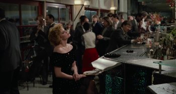 Movie still from “Working Girl” (1988), directed by Mike Nichols – A woman in a black dress standing in front of a counter; Medium shot, Over the shoulder angle