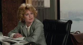 Movie still from “Working Girl” (1988), directed by Mike Nichols – A woman sitting at a desk in a room; Medium shot, Over the shoulder angle