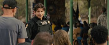 Movie still from “Wrong Turn” (2021), directed by Mike P. Nelson – A man in a police uniform standing in front of a crowd of onlookers; Medium shot, Over the shoulder angle