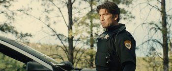 Movie still from “Wrong Turn” (2021), directed by Mike P. Nelson – A man in a police uniform standing next to a motorcycle; Medium shot, Over the shoulder angle
