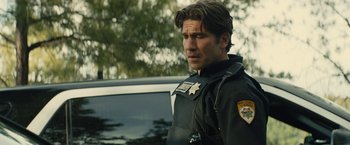 Movie still from “Wrong Turn” (2021), directed by Mike P. Nelson – A man in a police uniform standing next to a police car; Medium shot, Over the shoulder angle