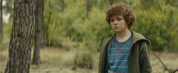 Movie still from “Wrong Turn” (2021), directed by Mike P. Nelson – A young boy standing in a field with trees in the background; Medium shot, Over the shoulder angle