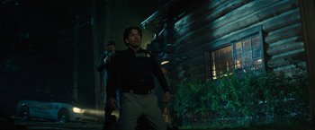 Movie still from “Wrong Turn” (2021), directed by Mike P. Nelson – A man standing next to another man holding a gun in front of a house; Medium shot, Over the shoulder angle