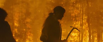 Movie still from “Wrong Turn” (2021), directed by Mike P. Nelson – A person holding a stick in front of a fire; Medium shot, Over the shoulder angle