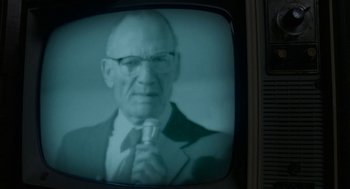 Movie still from “X” (2022), directed by Ti West – An old man with a tie and a suit is on a television screen; Extreme Close Up shot, Low angle