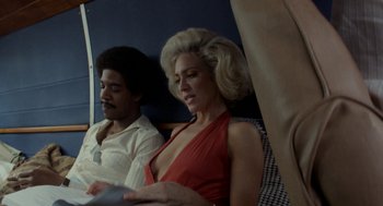 Movie still from “X” (2022), directed by Ti West – A man and a woman sitting next to each other on a train; Medium shot, Low angle