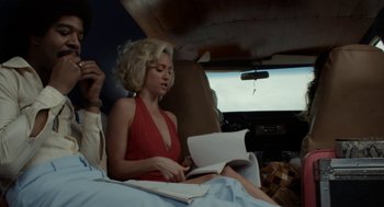 Movie still from “X” (2022), directed by Ti West – A woman sitting in the back of a car reading a book; Medium shot, Low angle