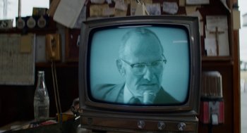 Movie still from “X” (2022), directed by Ti West – An older man in a suit and glasses is sitting in front of a television; Close Up shot, Low angle
