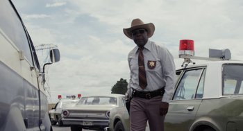 Movie still from “X” (2022), directed by Ti West – A man in a brown hat is standing next to a car; Medium shot, Low angle