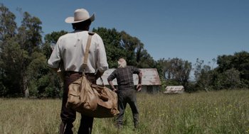 Movie still from “X” (2022), directed by Ti West – Two men standing in a field holding a bag; Wide shot, Low angle