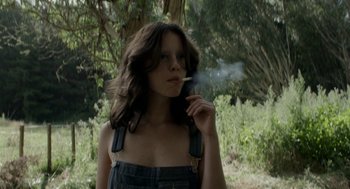 Movie still from “X” (2022), directed by Ti West – A woman in overalls is smoking a cigarette; Medium shot, Low angle