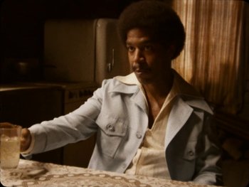 Movie still from “X” (2022), directed by Ti West – A man sitting at a table in front of an oven; Medium shot, Low angle