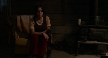 Movie still from “X” (2022), directed by Ti West – A woman sitting on a chair in a dark room; Medium shot, High angle