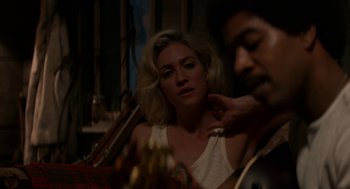 Movie still from “X” (2022), directed by Ti West – A woman sitting in front of a man with a guitar in front of him; Medium shot, Over the shoulder angle