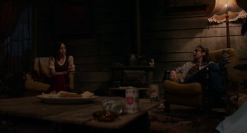 Movie still from “X” (2022), directed by Ti West – Two people sitting at a coffee table in a dark room; Wide shot, High angle