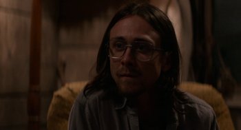Movie still from “X” (2022), directed by Ti West – A man with long brown hair wearing glasses; Close Up shot, Low angle