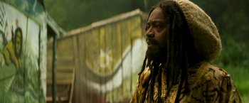 Movie still from “Yardie” (2018), directed by Idris Elba – A man with dreads is standing in front of a flag; Close Up shot, Low angle
