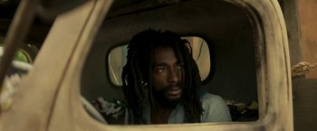 Movie still from “Yardie” (2018), directed by Idris Elba – A man with dreads sitting in the back of a vehicle; Close Up shot, Low angle