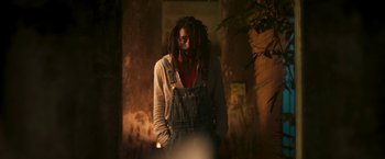 Movie still from “Yardie” (2018), directed by Idris Elba – A man with dreadlocks standing in front of a wall; Medium shot, Low angle