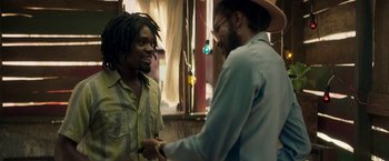 Movie still from “Yardie” (2018), directed by Idris Elba – Two men are shaking hands in front of a window; Medium shot, Over the shoulder angle