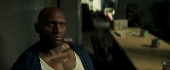Movie still from “Yardie” (2018), directed by Idris Elba – A bald man with a gold chain around his neck; Close Up shot, Over the shoulder angle