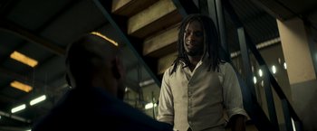 Movie still from “Yardie” (2018), directed by Idris Elba – A man with dreads standing next to a person; Medium shot, Over the shoulder angle