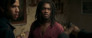 Movie still from “Yardie” (2018), directed by Idris Elba – A person with dreadlocks wearing a red shirt; Close Up shot, Over the shoulder angle