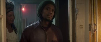 Movie still from “Yardie” (2018), directed by Idris Elba – A man wearing a green hat and a brown jacket; Close Up shot, Over the shoulder angle