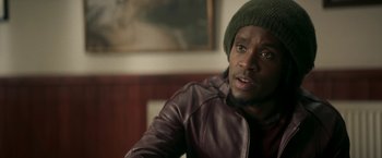 Movie still from “Yardie” (2018), directed by Idris Elba – A person wearing a jacket and a hat; Close Up shot, Over the shoulder angle