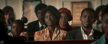 Movie still from “Yardie” (2018), directed by Idris Elba – A woman sitting in front of two other people; Medium shot, Over the shoulder angle