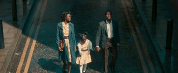 Movie still from “Yardie” (2018), directed by Idris Elba – A man , woman , and a little girl are holding hands; Medium shot, High angle