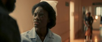 Movie still from “Yardie” (2018), directed by Idris Elba – A woman in a nurse's uniform looking up; Close Up shot, Low angle