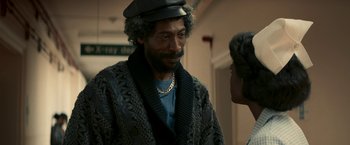 Movie still from “Yardie” (2018), directed by Idris Elba – A man wearing a hat and a sweater talking to another man; Close Up shot, Over the shoulder angle