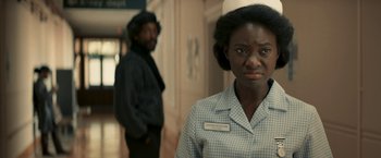 Movie still from “Yardie” (2018), directed by Idris Elba – A woman standing next to a man in a hallway; Close Up shot, Over the shoulder angle