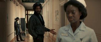 Movie still from “Yardie” (2018), directed by Idris Elba – A man standing in a hallway next to a woman; Medium shot, Over the shoulder angle