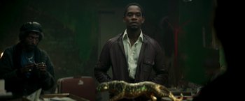 Movie still from “Yardie” (2018), directed by Idris Elba – A man standing in front of an alligator; Medium shot, Low angle