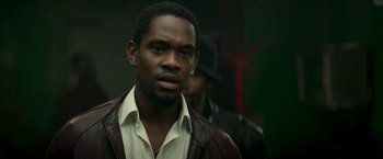 Movie still from “Yardie” (2018), directed by Idris Elba – A man wearing a brown jacket and a white shirt; Close Up shot, Low angle