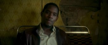 Movie still from “Yardie” (2018), directed by Idris Elba – A man wearing a brown leather jacket and a white shirt; Close Up shot, Low angle