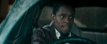 Movie still from “Yardie” (2018), directed by Idris Elba – A man sitting in the driver's seat of a car; Close Up shot, Over the shoulder angle