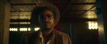 Movie still from “Yardie” (2018), directed by Idris Elba – A person wearing glasses and a hat; Close Up shot, Low angle