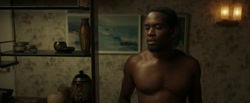 Movie still from “Yardie” (2018), directed by Idris Elba – A man with no shirt is standing in a room; Medium shot, Low angle