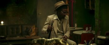 Movie still from “Yardie” (2018), directed by Idris Elba – A man in a hat and glasses holding an umbrella; Medium shot, Low angle