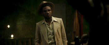 Movie still from “Yardie” (2018), directed by Idris Elba – A man wearing a hat and a jacket; Medium shot, Low angle