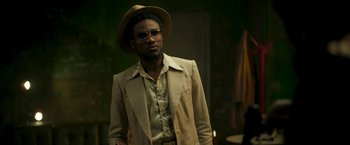 Movie still from “Yardie” (2018), directed by Idris Elba – A man wearing a hat and a jacket; Medium shot, Low angle