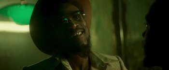 Movie still from “Yardie” (2018), directed by Idris Elba – A person with a beard wearing glasses; Close Up shot, Low angle