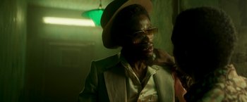 Movie still from “Yardie” (2018), directed by Idris Elba – A man in a hat and glasses is posing for a picture; Close Up shot, Over the shoulder angle