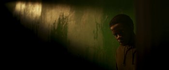 Movie still from “Yardie” (2018), directed by Idris Elba – A man standing against a green wall in a room; Close Up shot, Low angle